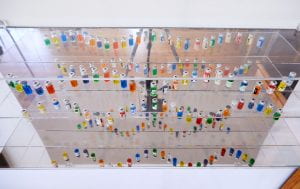 Saline solution bottles (from Copaxone treatment), filled with brightly colored liquid mounted on clear Plexiglas shelves.