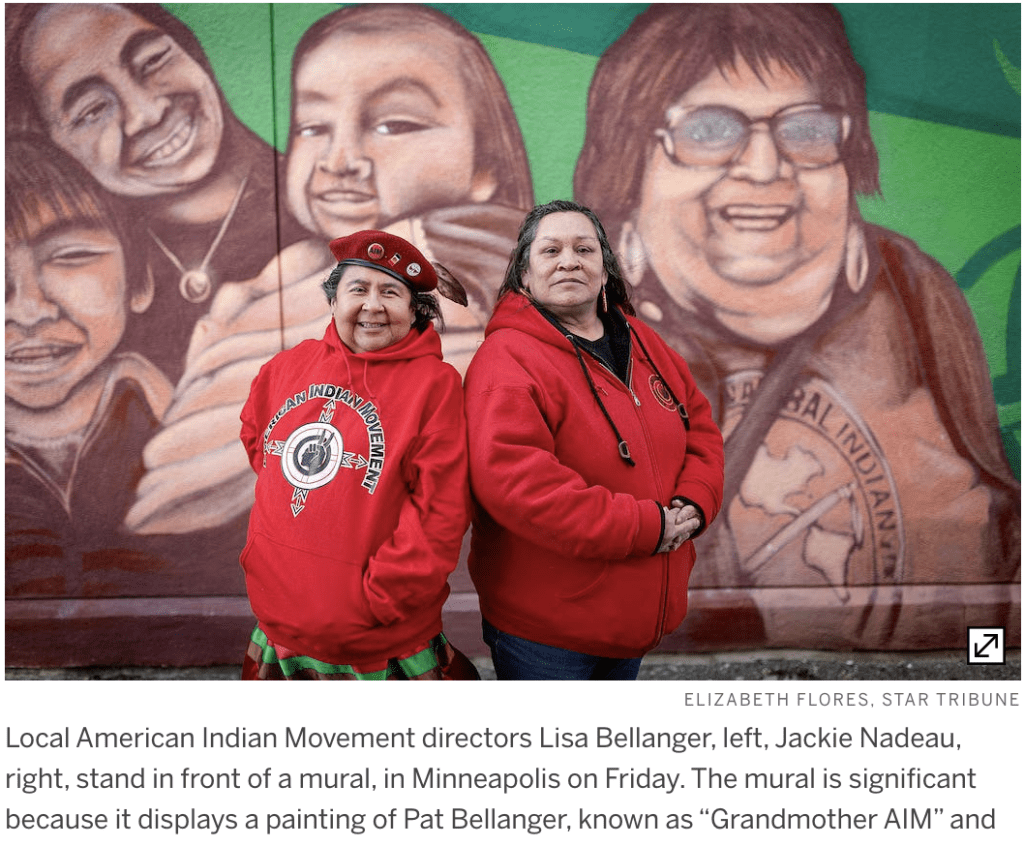 Image of two Native women Lisa Bellanger, and Jackie Nadeau standing in front of a mural in Minneapolis on Friday. The mural is significant because it displays a painting of Pat Bellanger known as "Grandmother AIM" .