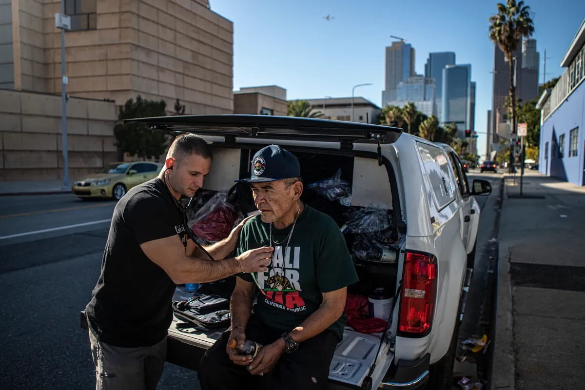 Physician Assistant Brett Feldman does a checkup on his patient Gary Dela Cruz on the side of the road near his encampment in downtown Los Angeles on Nov. 18, 2022.